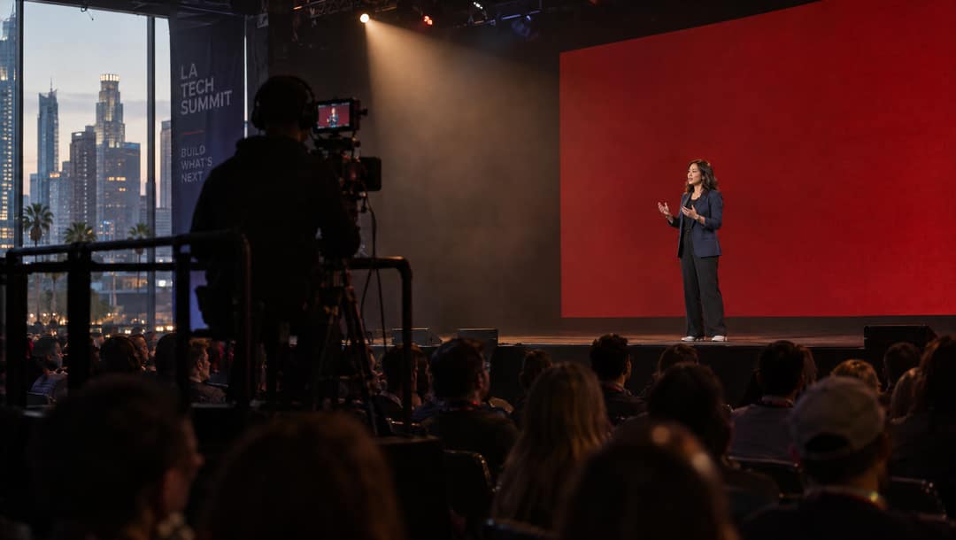 Speaker on a dark stage under a spotlight with a red screen behind her